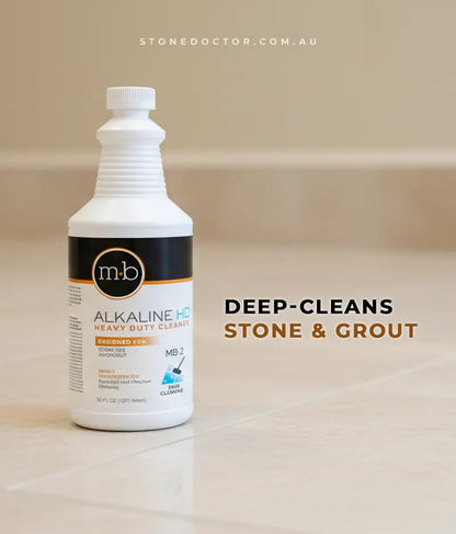 Bottle of m-b Alkaline HD Heavy Duty Cleaner on a tiled floor with text 'DEEP-CLEANS STONE & GROUT'.